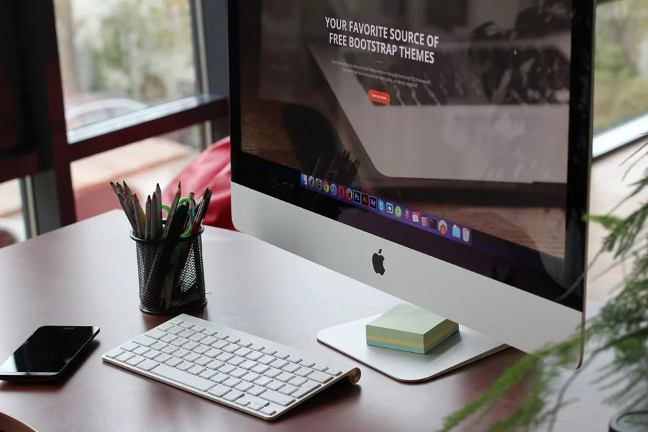 Close-up of a silver laptop and smartphone on a wooden desk, capturing modern work essentials.